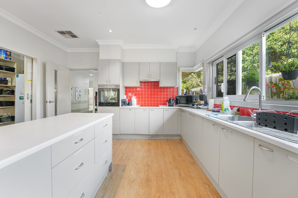 Spacious kitchen with island bench, red tiled splashback and large windows.