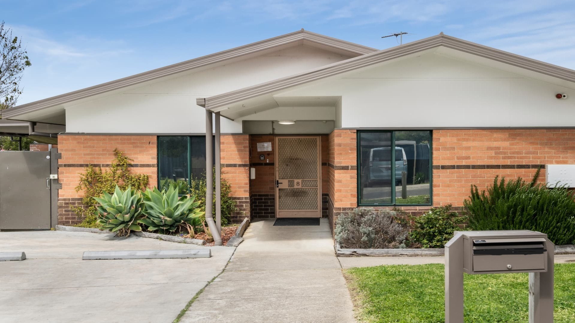 --Front of Bundoora house. Brick facade with a concrete path leading to the front door.--