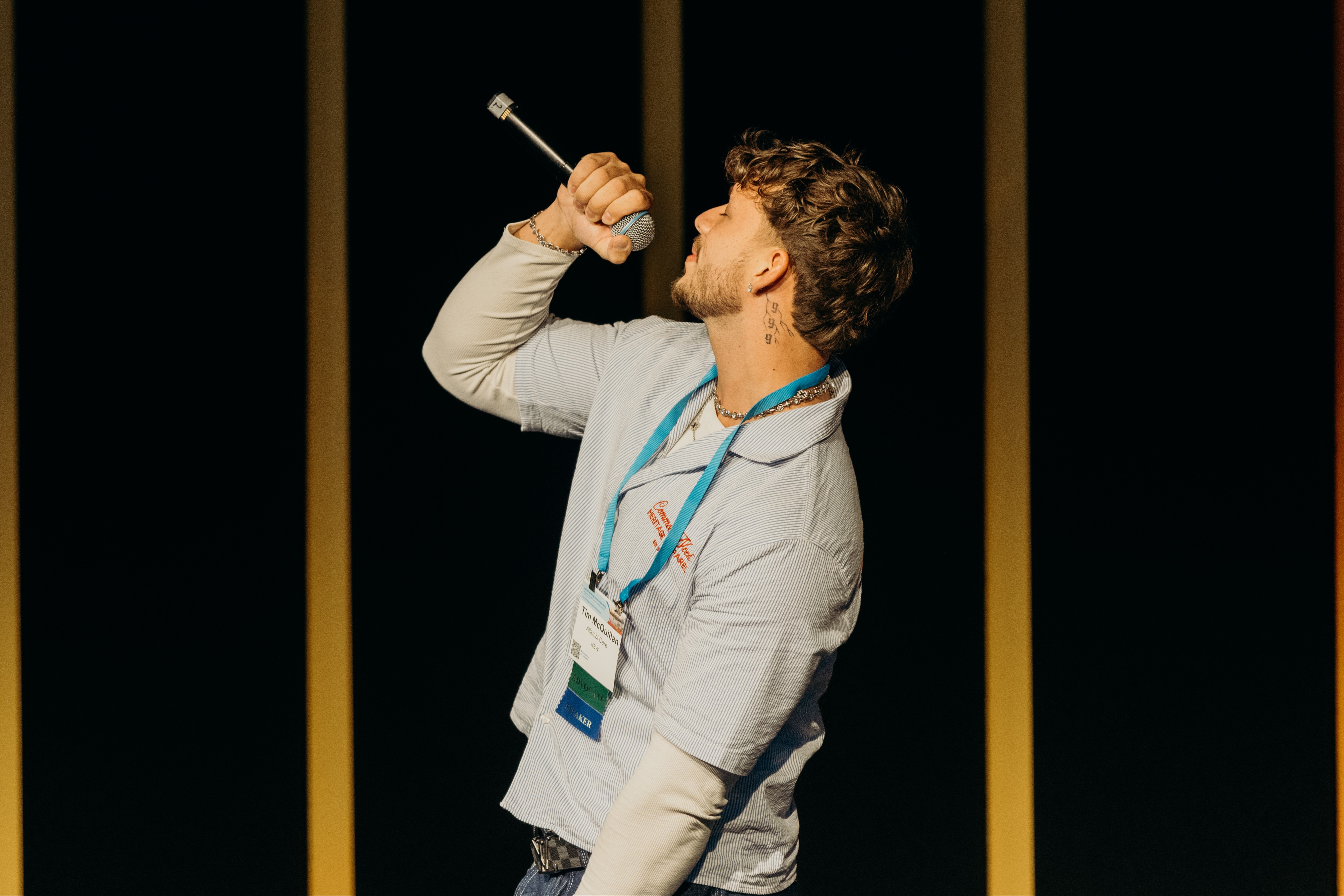 Tim is on stage singing. He is wearing a polo shirt, leaning back and holding a microphone. 