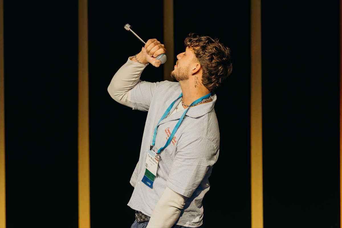 Tim is on stage singing. He is wearing a polo shirt, leaning back and holding a microphone.