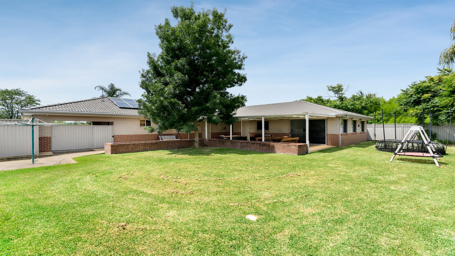 Backyard with large grassed area, a swing set and a trampoline.
