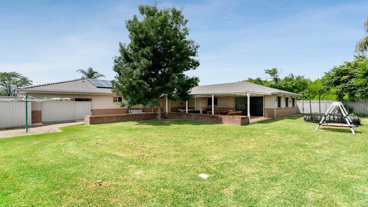 Backyard with large grassed area, a swing set and a trampoline.
