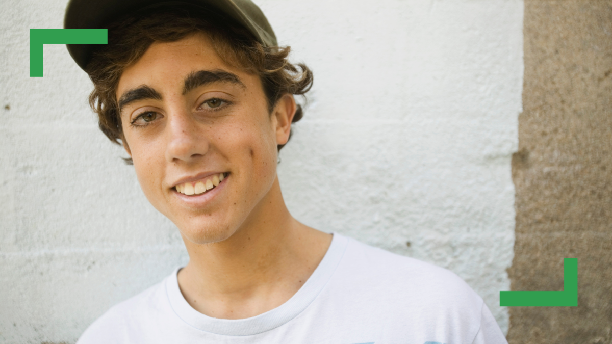 A teenage boy with short brown hair wearing a green cap and a white t-shirt.