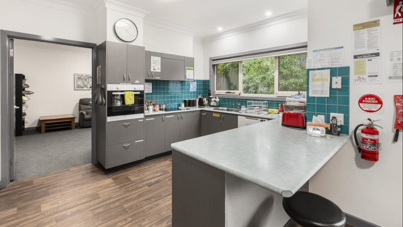 A kitchen with grey cabinets, blue tiles, an oven, stove, dishwasher and a bench with stool seating.