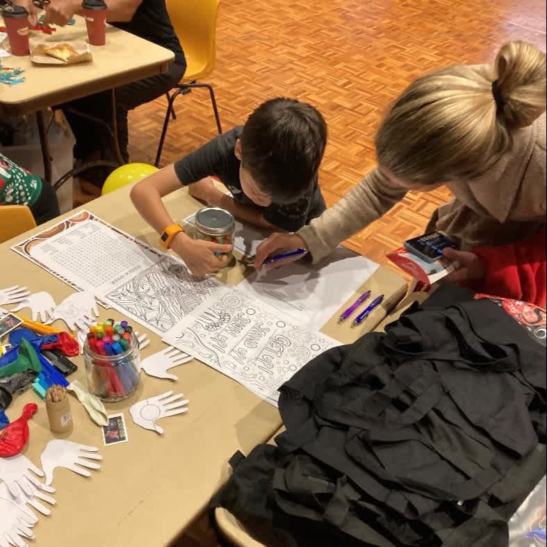 A young boy and his mother are doing an activity with paper and pens on a table.