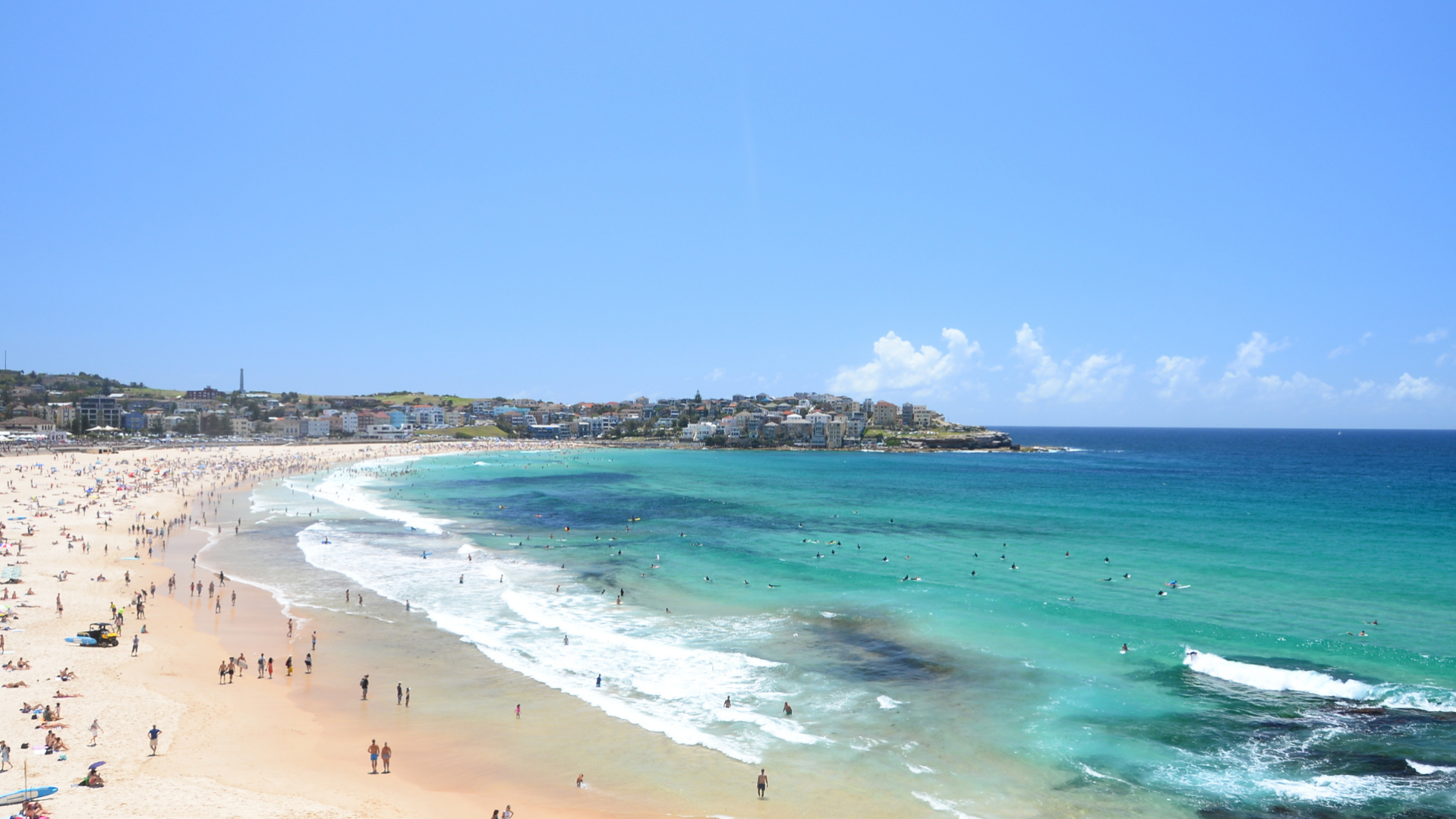 --Image of Bondi Beach with 100s of people sitting on the sand and swimming in the ocean.--
