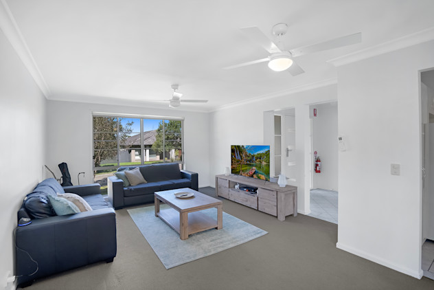 Living room with blue lounges coffee table, tv unit and ceiling fans