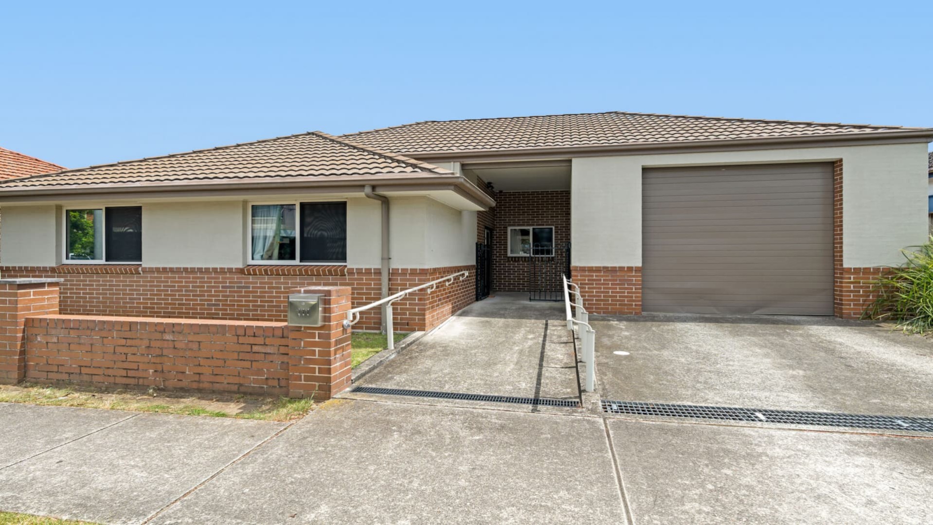 front of red brick house, with concrete walkway, grab rails and concrete entry to single garage.