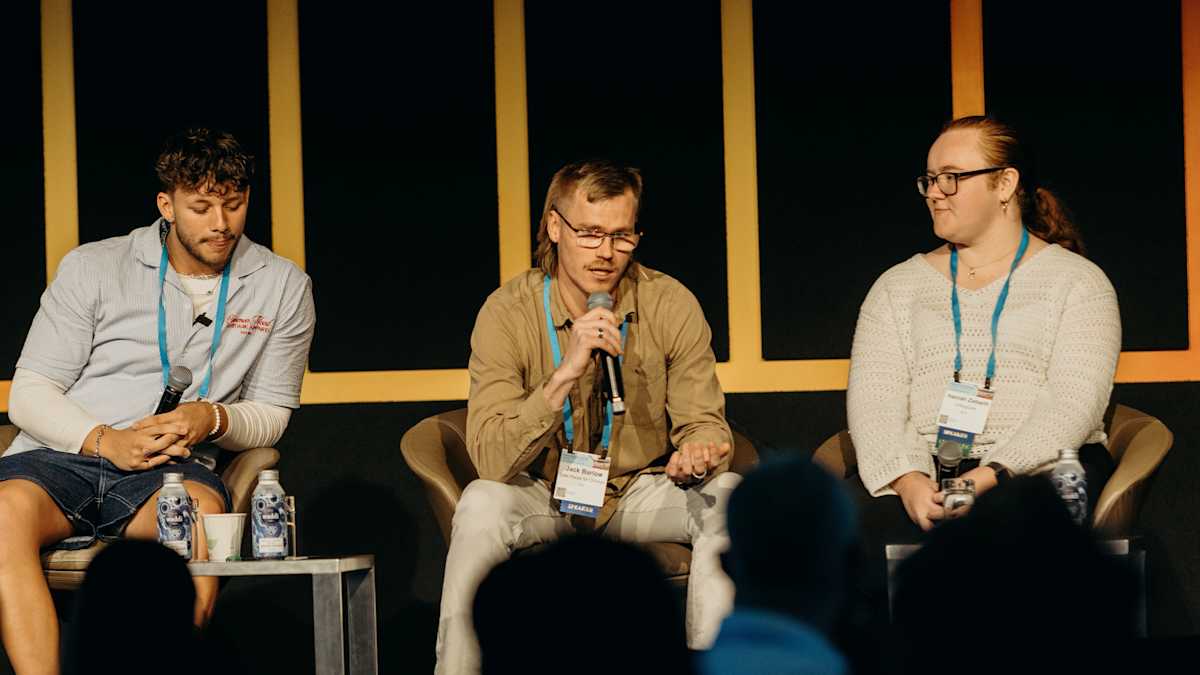 Three youth advocates sitting on stage. Jack, in the centre, is holding the microphone and speaking.