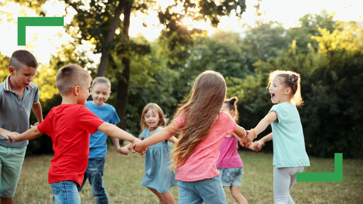Children hold hands in a circle outdoors.