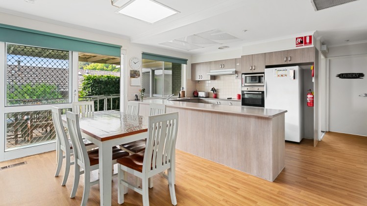 --Dining area with a wooden table and six chairs. Next to the dining area is the kitchen with ample bench space.--