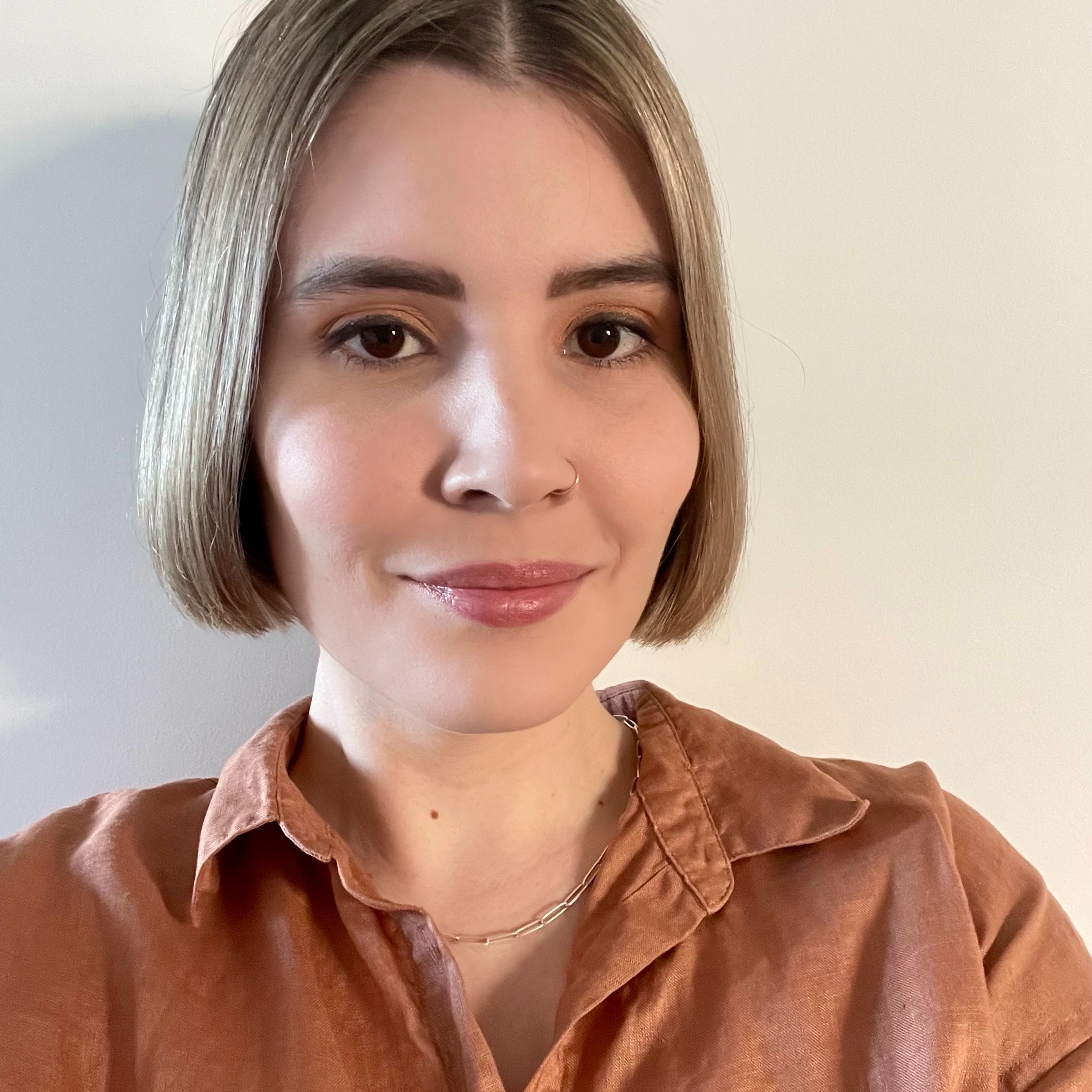Close-up of Ashleigh with short blonde hair, wearing a brown shirt and smiling at the camera.