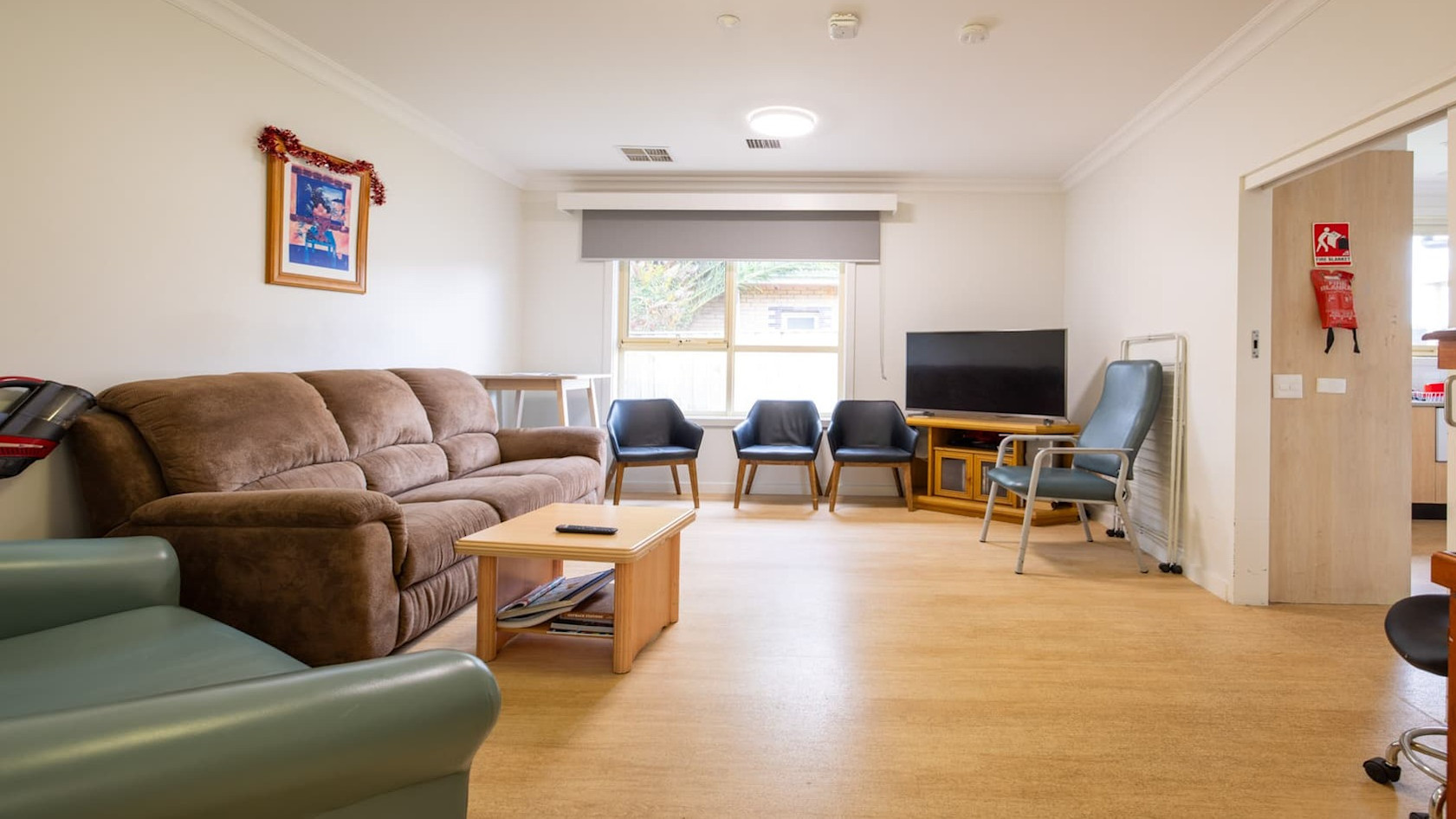 Second living space with brown lounge, armchair and soft chairs facing window and television.