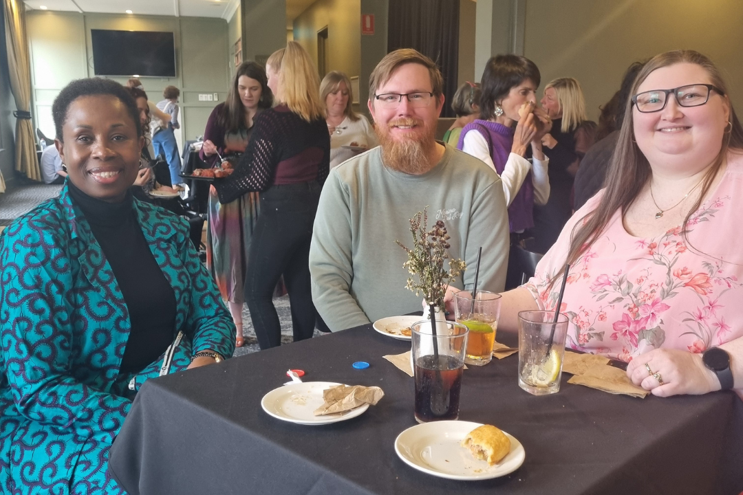 Three carers sitting at a table, smiling at the camera.