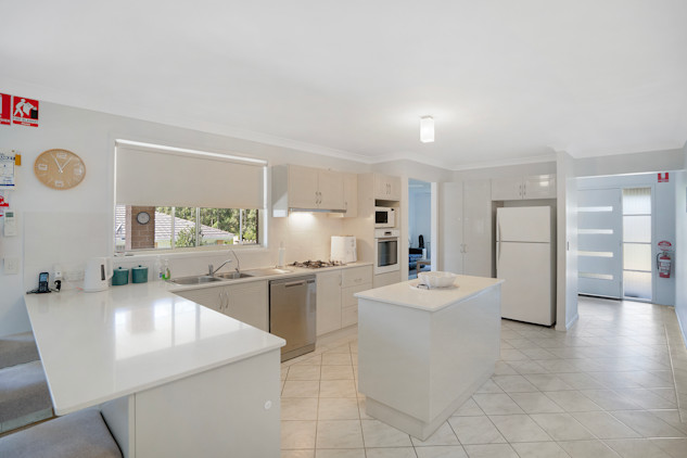 Open-plan kitchen with white bench tops and cupboard and and island bench