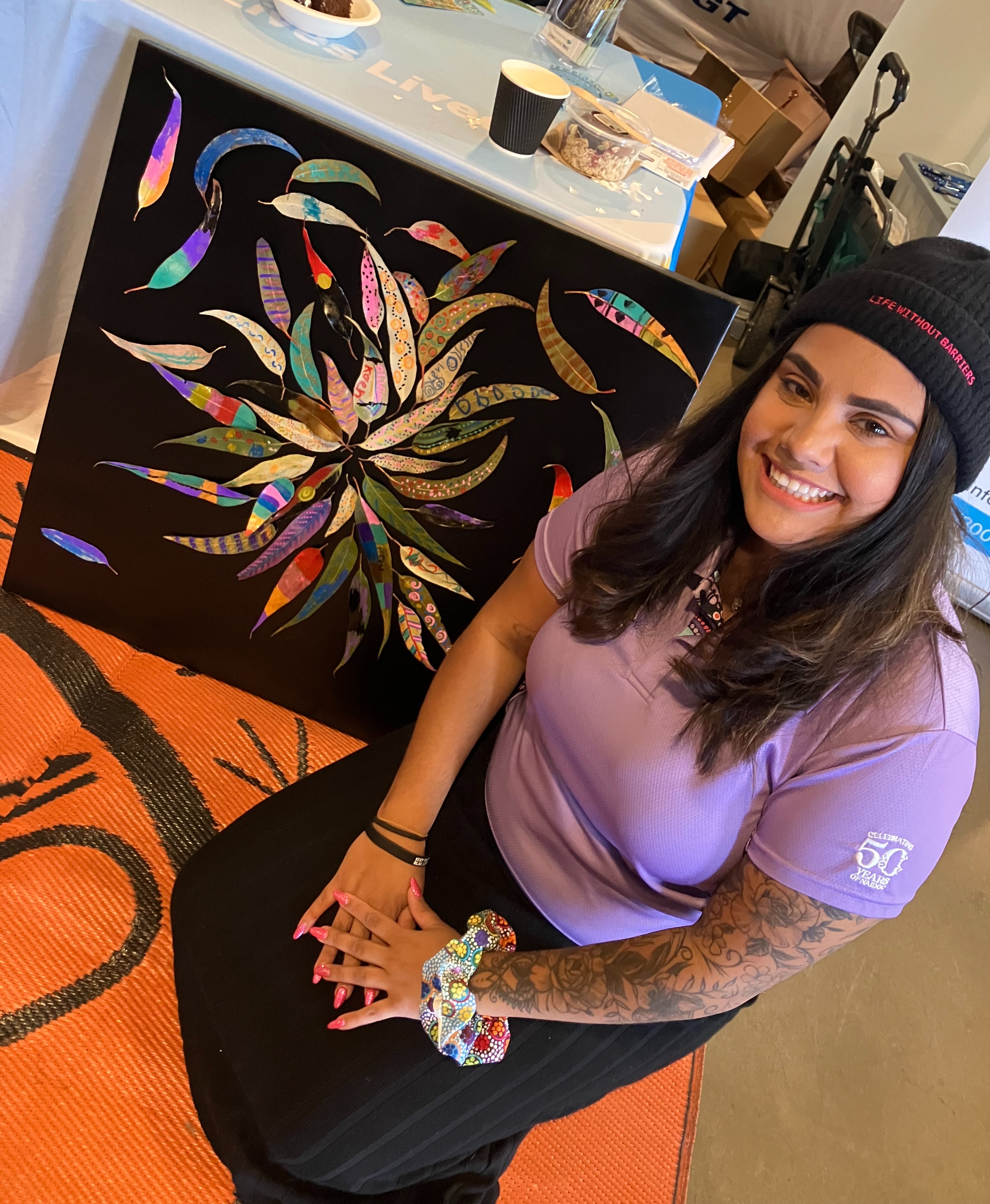 Chloe sits beside an artwork created by attendees, smiling at the camera.