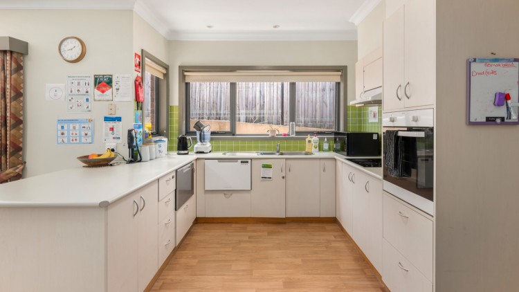 --Wrap around white kitchen with green tiles, window, wooden floors.--