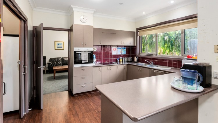 Wrap around kitchen with wooden floors, purple tiles and light counters. Backyard can be seen through kitchen window.