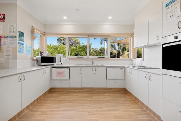 Bright accessible kitchen with large windows, double sink, and white cupboards.