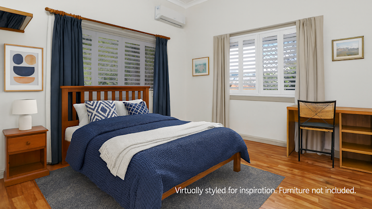 Bedroom with wooden bed, navy bedding, side table with lamp, desk, and artwork, featuring large shuttered windows.