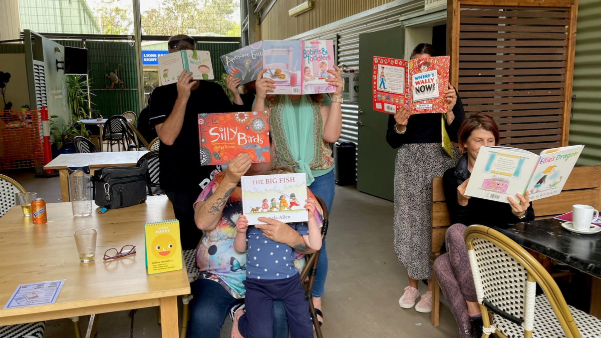 People holding books over their faces at the carer's morning tea.