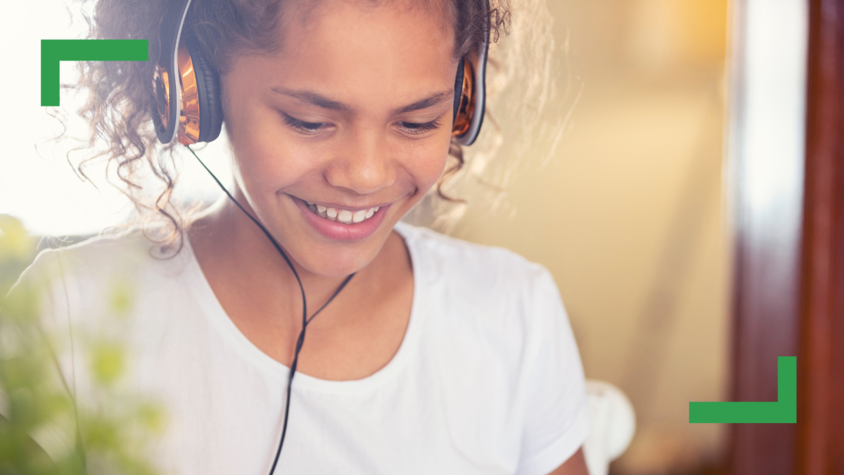 An Aboriginal teenage girl with curly brown hair in a pony tail is wearing headphones and a white shirt.