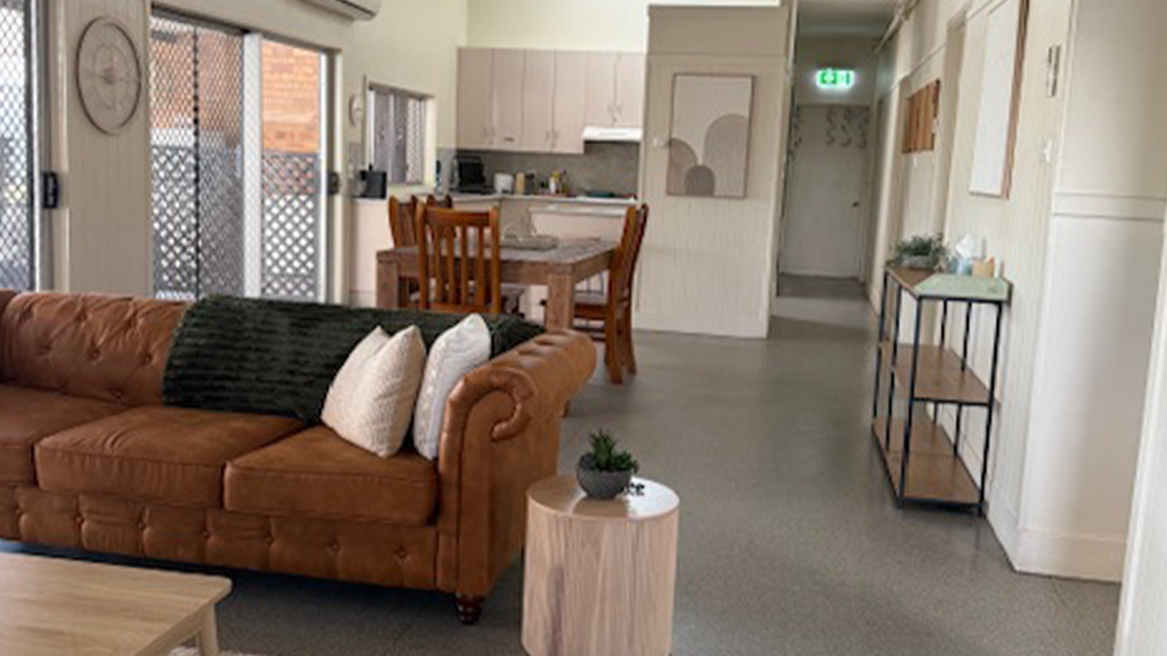 Open-plan living and dining area with a warm, inviting feel, including a leather couch, timber dining set, and kitchen in the background.