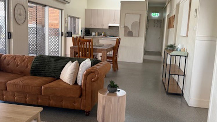 Open-plan living and dining area with a warm, inviting feel, including a leather couch, timber dining set, and kitchen in the background.