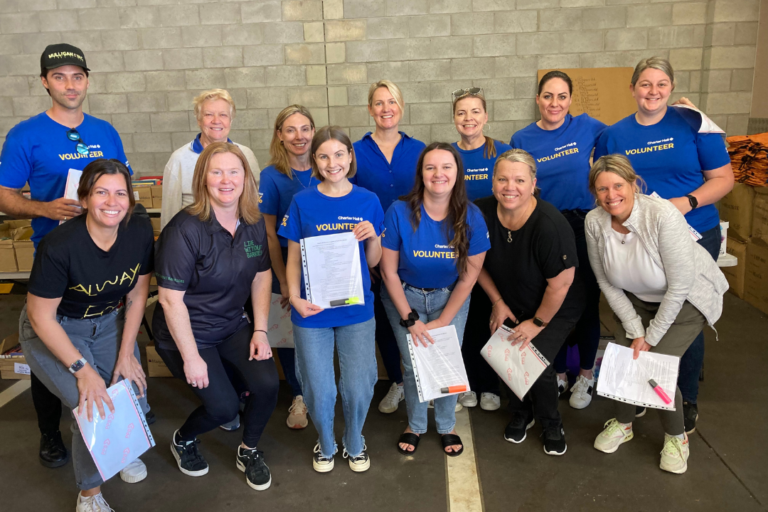 A group of staff and volunteers at the Book Backpack Packing Day, smiling at the camera.