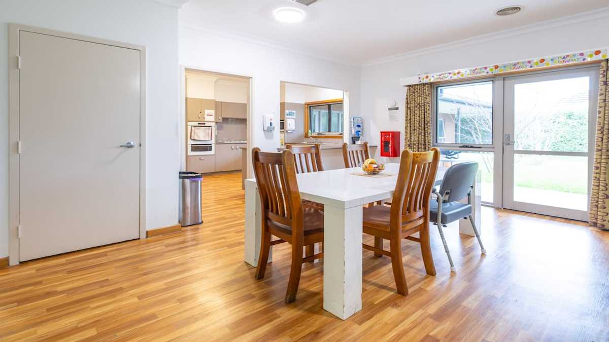 White dining table on hard wooden flooring with five chairs looking into the kitchen.