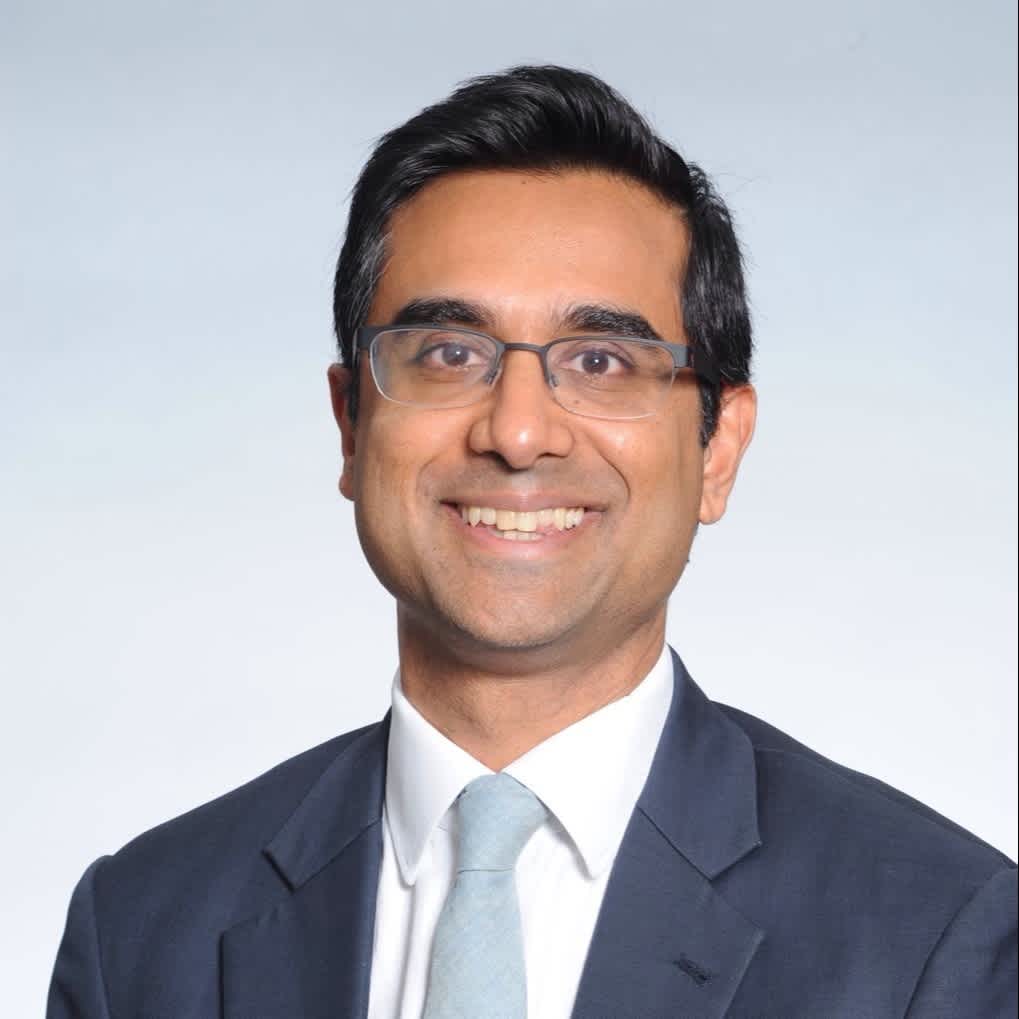 Mr. Rajiv Viswanathan is wearing a white shirt, light blue tie, dark blue suit. He has glasses and is smiling