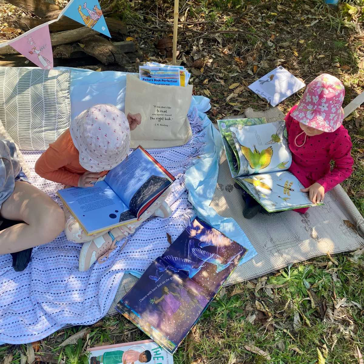 Children sitting on picnic rugs reading picture books.