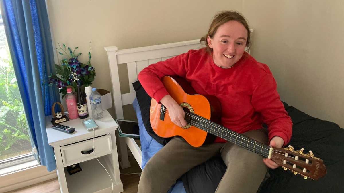 Cassie in a red jumper playing the guitar.