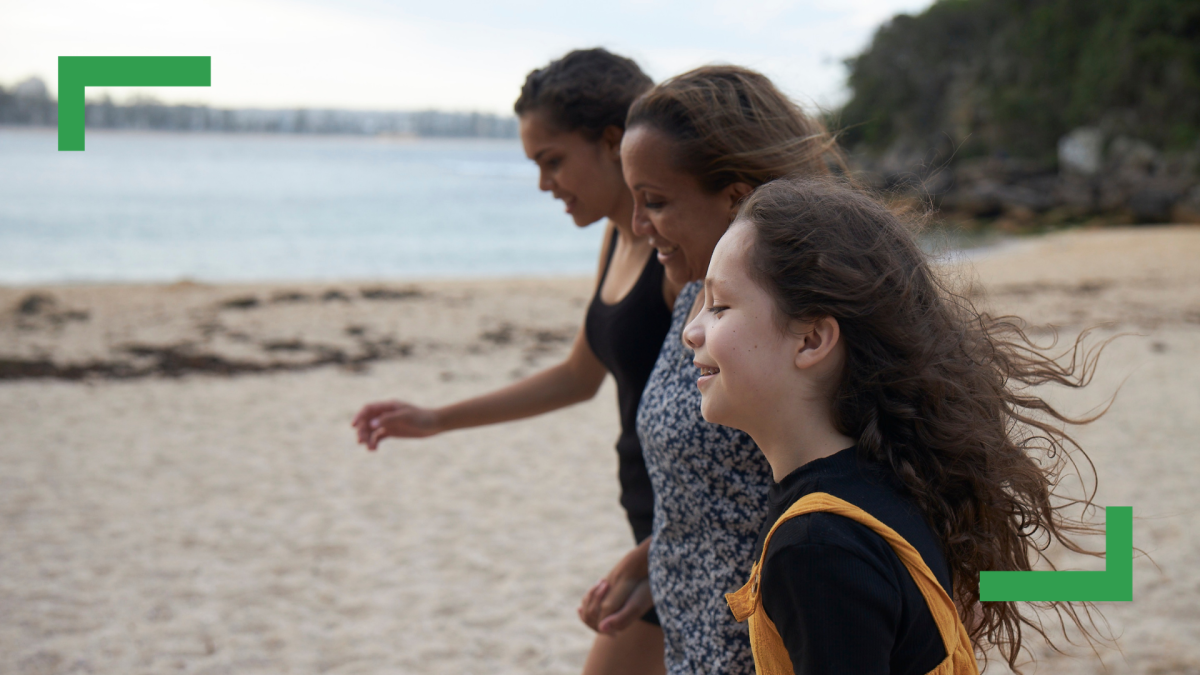 A mother and her two daughters walking in a line on a beach.
