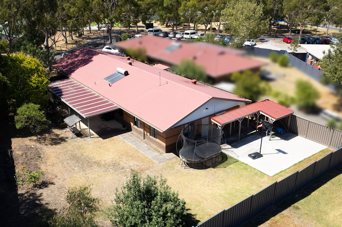 Aerial view of backyard, with large grassed area, undercover patio, trampoline and basketball hoop.
