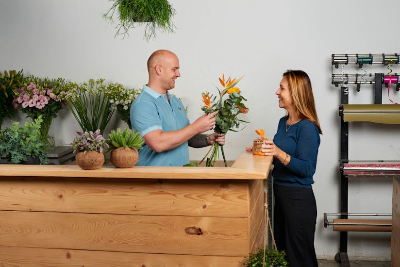 Blomsterhandler med kunde ved skranken