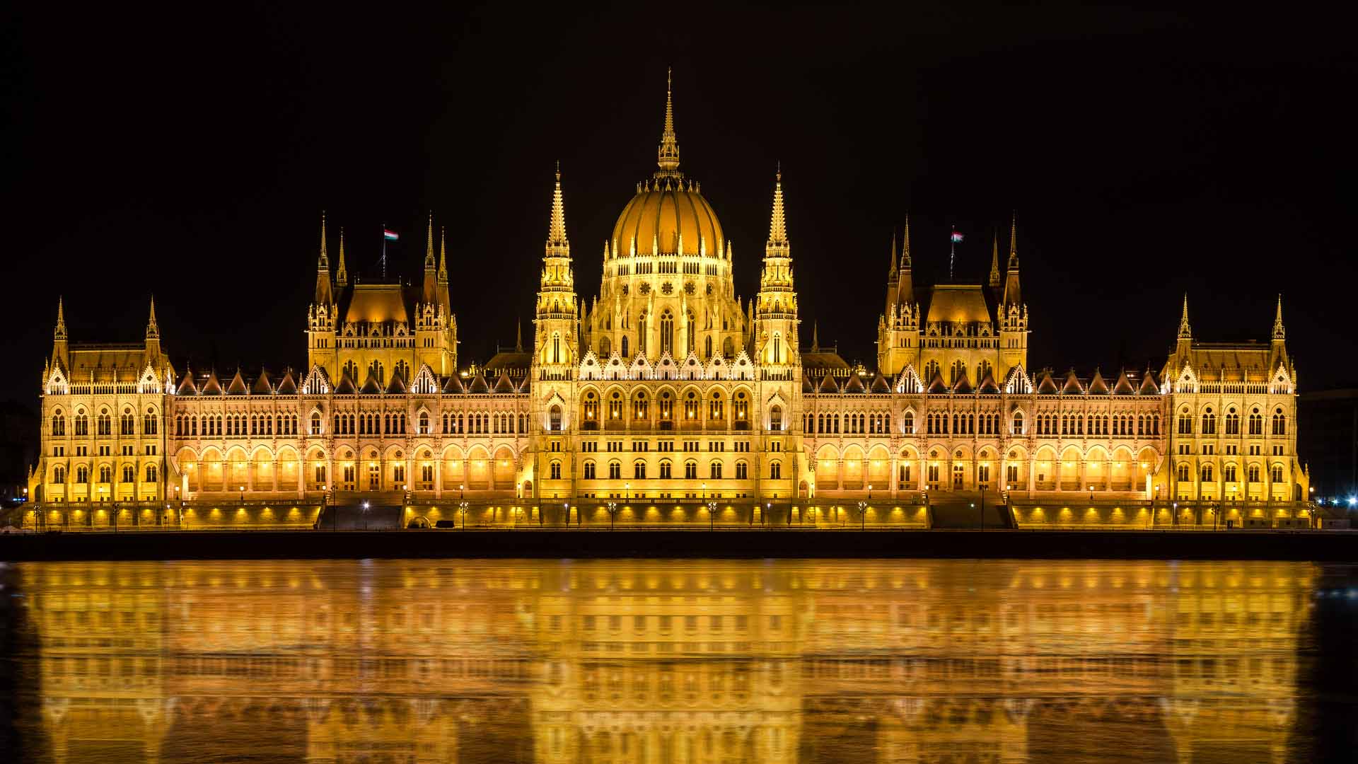 Illuminated Budapest parliament building at night with dark sky and reflection in Danube river