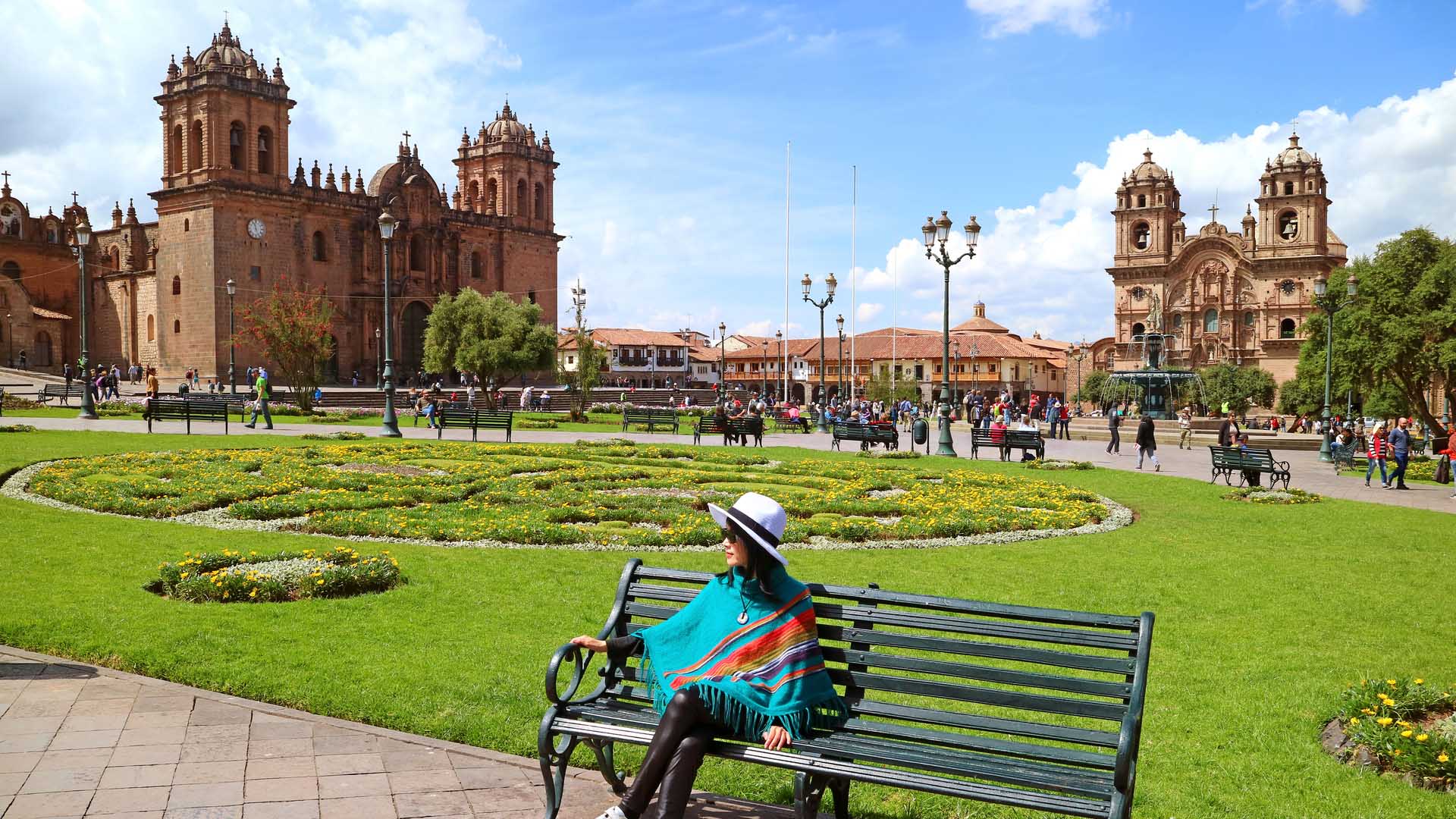 Female-relaxing-on-a-bench-at-Plaza-de-Armas-with-Cusco-Cathedral-and-the-Iglesia-de-la-Compania-de-Jesus-in-backg