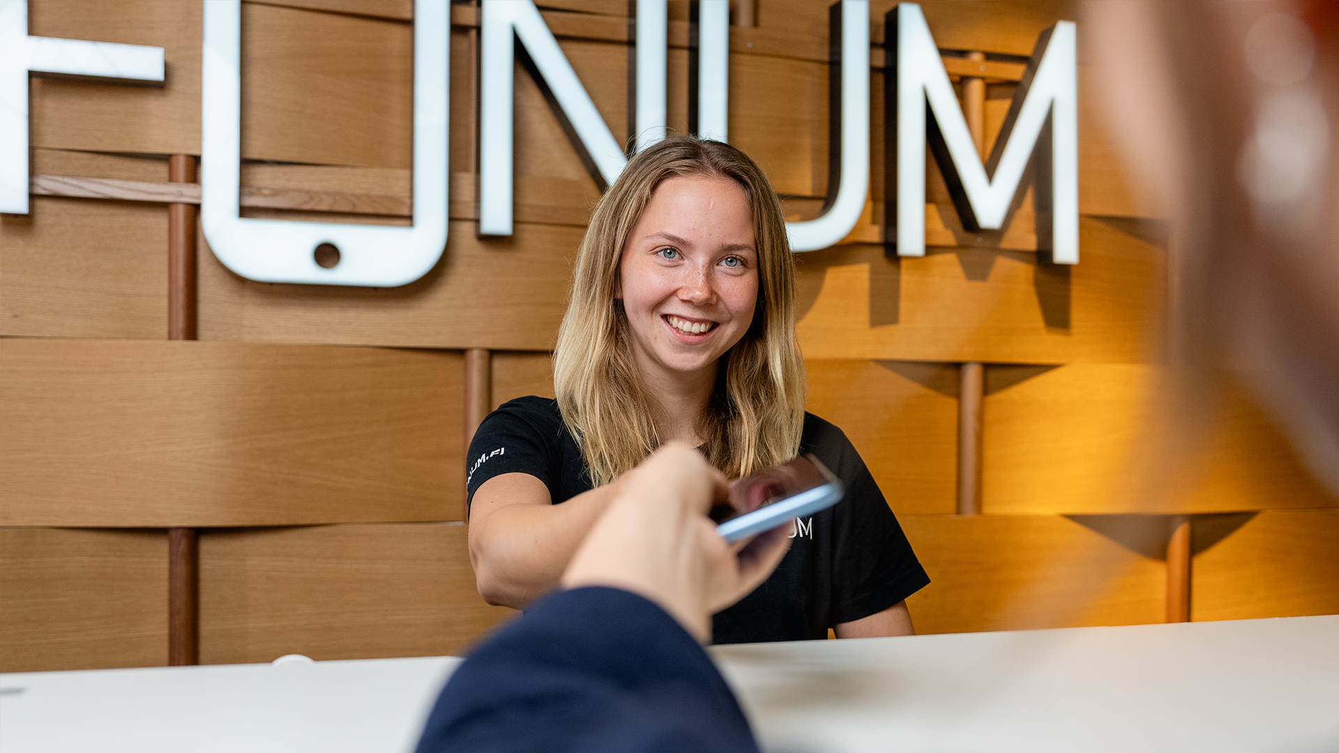 Fonum naistyöntekijä ojentaa huollettua puhelinta asiakkaalle