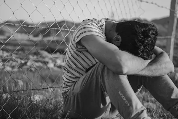 Immigrant boy against a fence. Photo by Mojtaba Ravanbakhsh on Unsplash.

