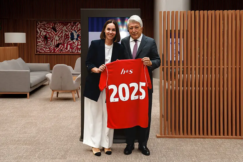 Directora de Comunicación de h&s y Presidente del Atlético de Madrid sosteniendo la camiseta del equipo del Atlético de Madrid roja con el nombre “h&s” y número 22.