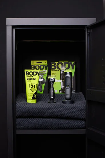 Productos GilletteLabs Body colocados sobre toallas negras dentro de un armario oscuro abierto.
