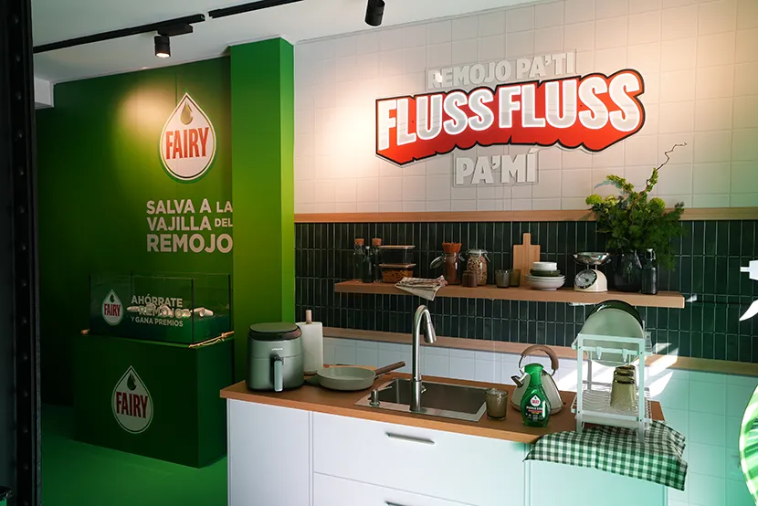 Fondo de cocina con paredes verdes, estampilla de Fairy, utensilios de cocina y un fregadero con platos.