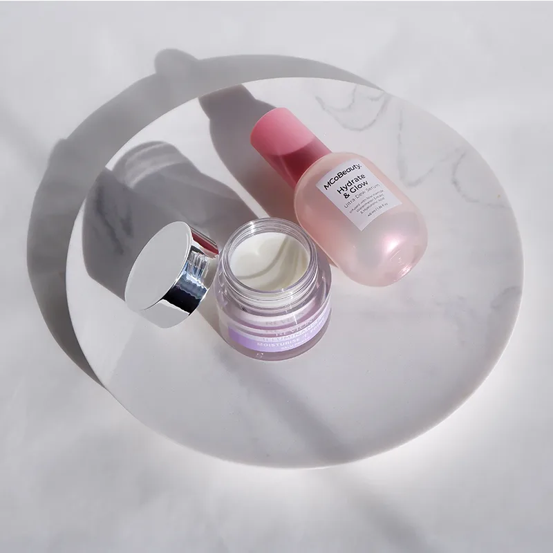 Pink skincare products on white marble surface with dramatic circular shadow, featuring cream jar and serum bottle.