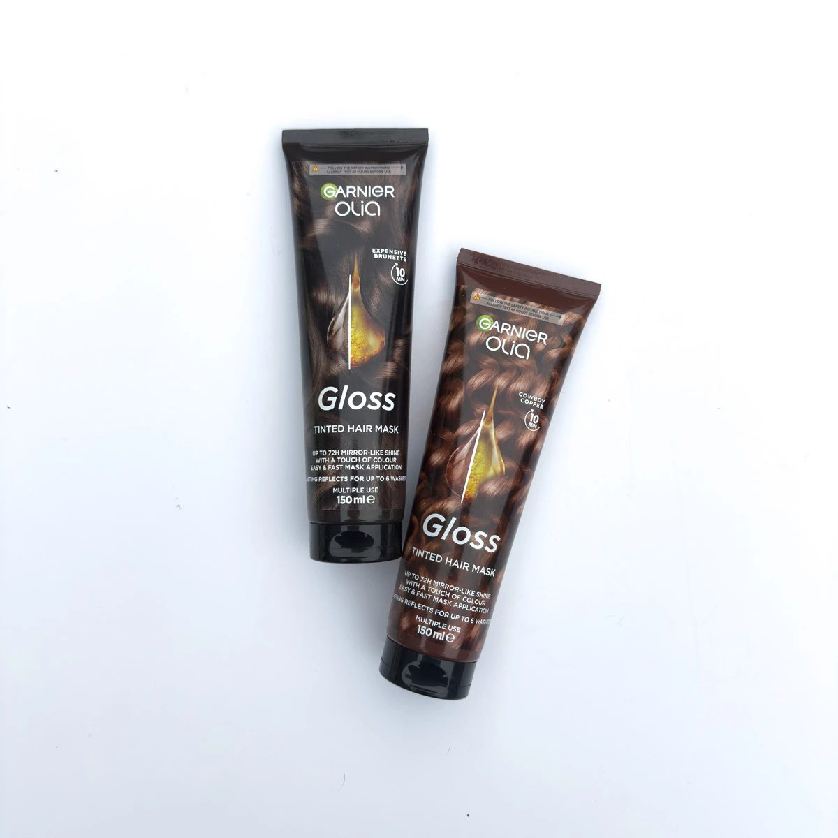 Two Garnier Olia Gloss Tinted Hair Mask tubes in dark packaging, shades Expensive Brunette and Cowboy Copper, 150ml each.