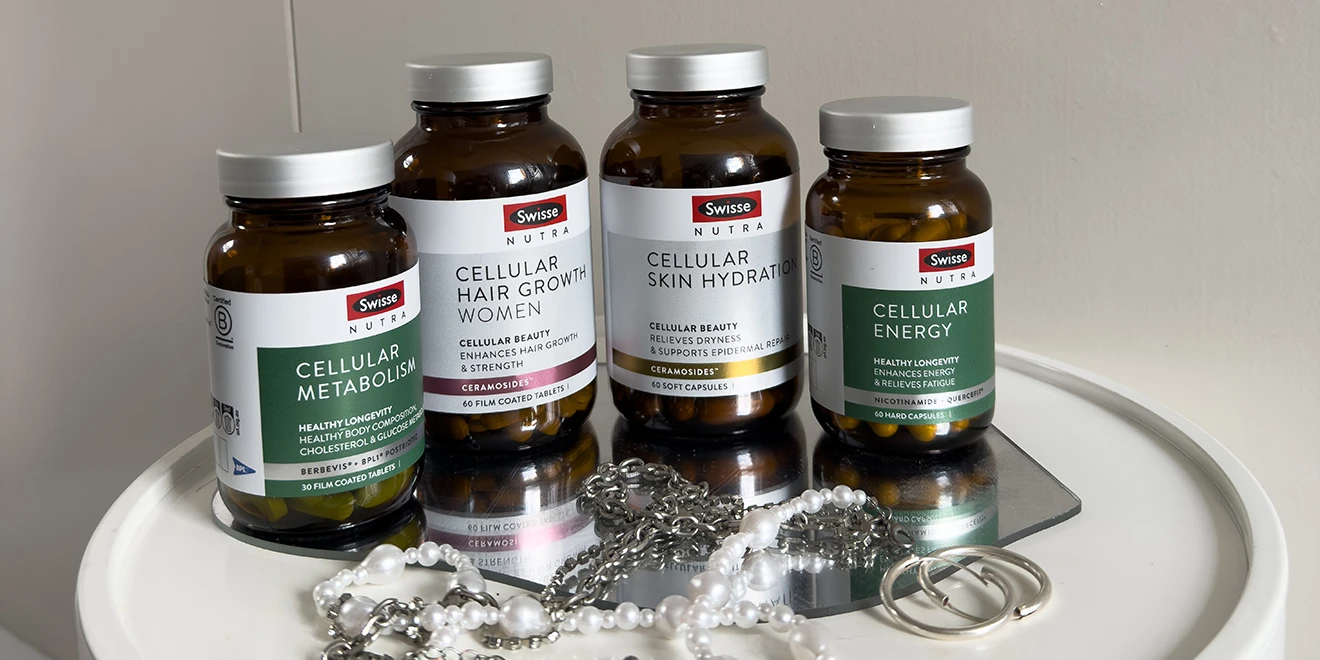 Four Swisse Nutra supplement bottles for cellular health, including metabolism, hair growth, skin hydration, and energy, with pearl necklace below
