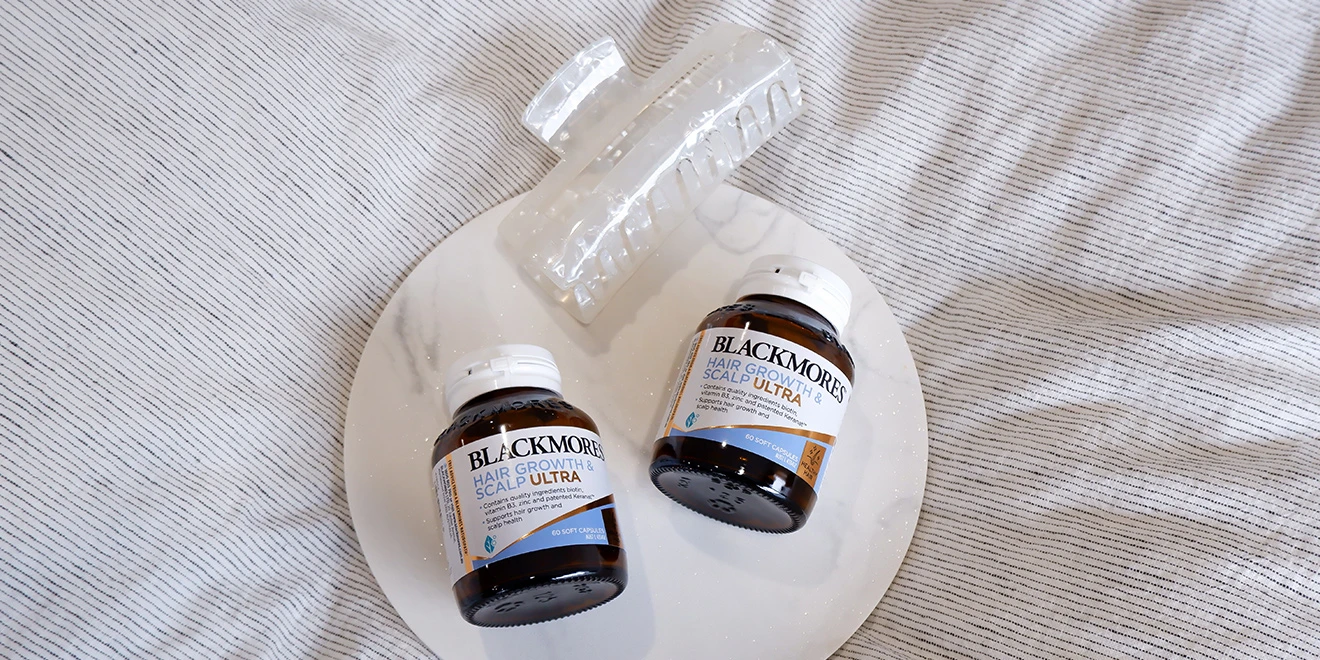 Two bottles of Blackmores Hair Growth Scalp Ultra supplements on a white plate against a gray striped fabric background