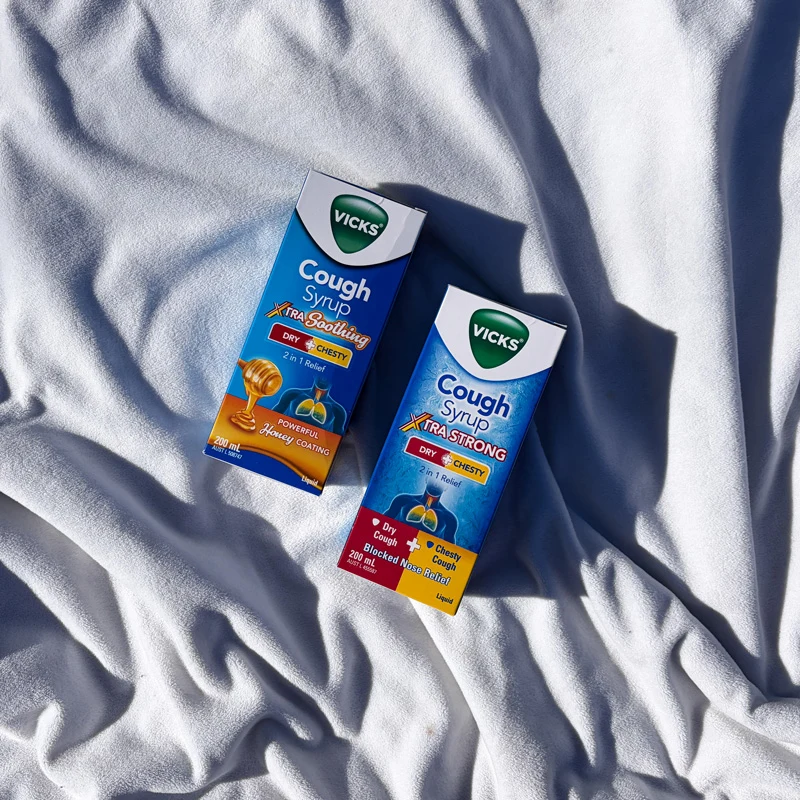 Two Vicks Cough Syrup boxes, Xtra Soothing and Xtra Strong, placed on white fabric in sunlight.