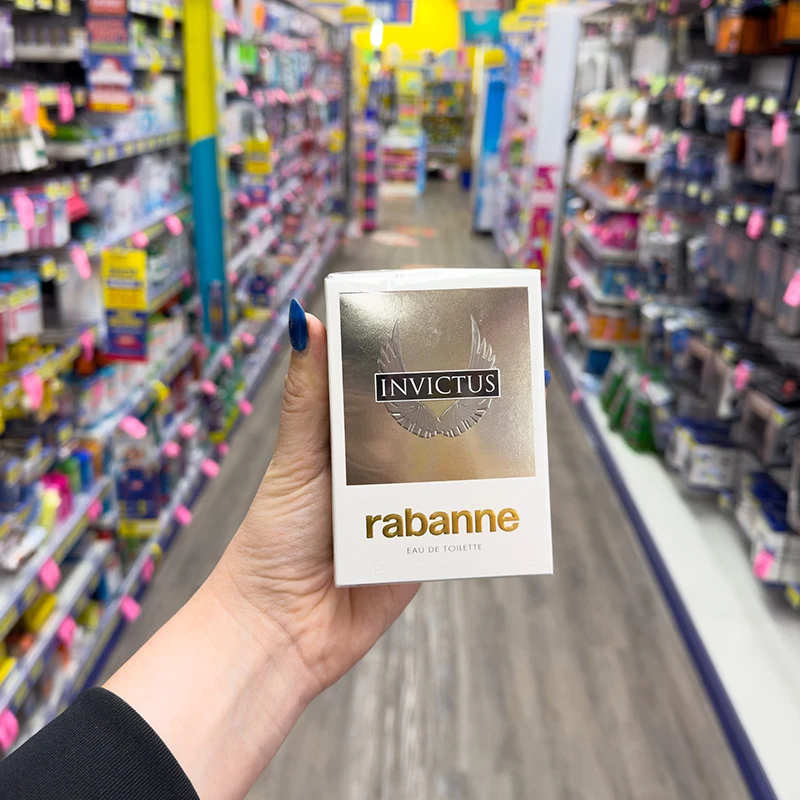 Hand holding Invictus by Rabanne perfume in retail store aisle with product displays in background