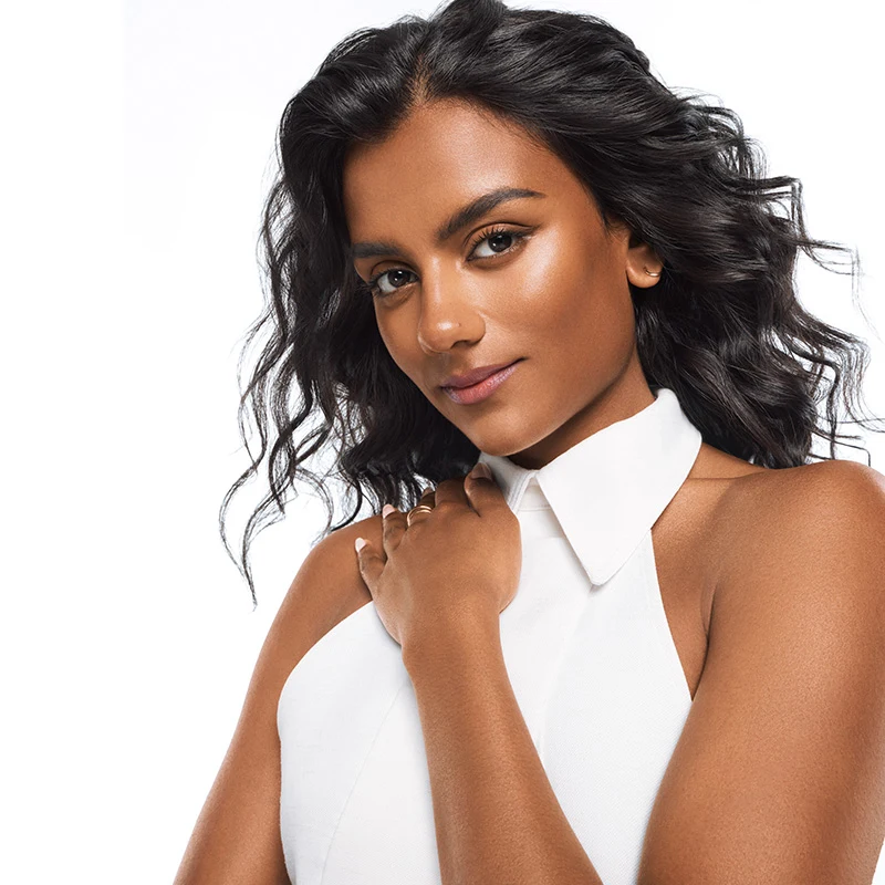 Close-up beauty portrait of a woman with wavy black hair and glowing skin, wearing a white halter top against a white background